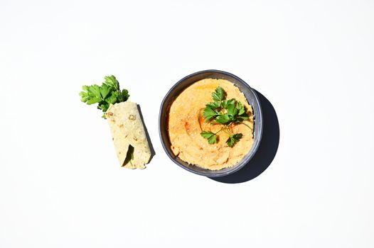 Flat lay composition with green parsley wrapped in pita bread and a bowl of chickpea hummus, sprinkled with paprika isolated on white background with copy space for advertising text