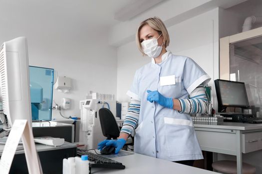Female doctor in coat lab and mask using a computer in a hospital office