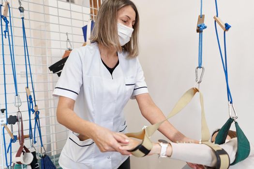 Female physiotherapist with a facial mask using a sling during rehabilitation therapy with a patient