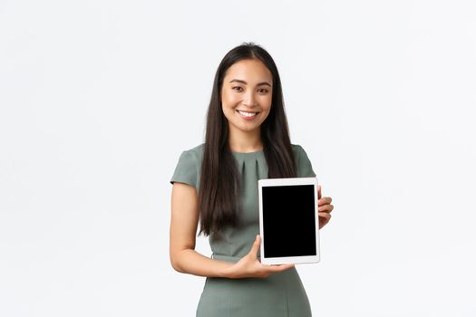 Smiling cheerful asian woman open own fashion store online, showing digital tablet screen with pleased and proud expression, introduce application, recommend click link, white background.