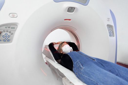 Patient with a protective facial mask into a tomography machine in an hospital