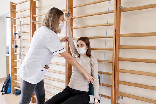 Physiotherapist working with a patient using ropes and parallel bars in a rehabilitation room