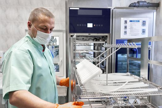 Man wearing gloves using a machine to sterilising medical supplies in an hospital