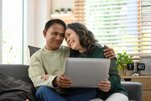 Loving senior couple relaxing on couch and using laptop, spending time together at home.