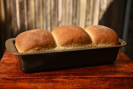 Close-up of a baking dish with freshly baked hot whole grain bread, on a rustic wooden background with copy ad space for advertising text. Still life. Food composition. Flat lay