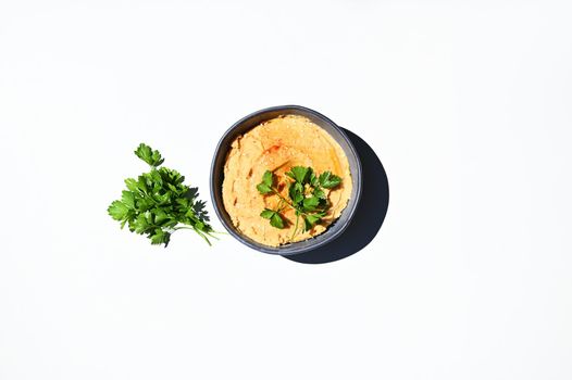 Flat lay composition with green parsley and a bowl with topped chickpea hummus, sprinkled with paprika, isolated over white background with copy space for advertising text