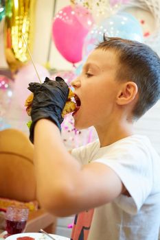 The handsome little boy eating burger in black rubber gloves