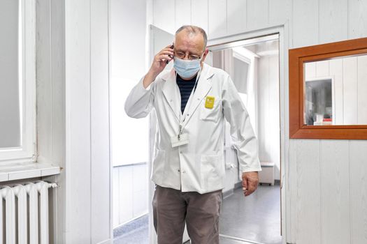 Aged doctor with a mask talking with a mobile in an hospital