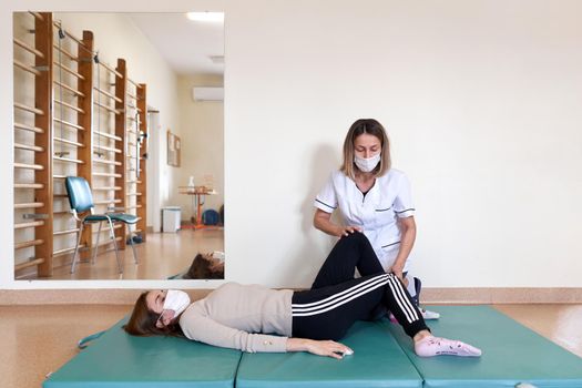 Physiotherapist doing rehabilitation exercises on a patient's leg on a mat