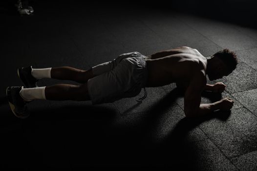 Shirtless african american man doing an elbow plank in the gym