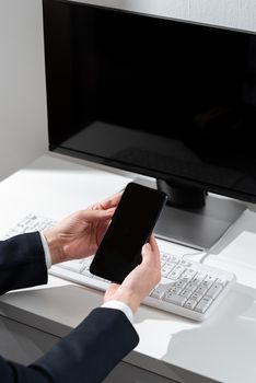 Businesswoman Holding Mobile Phone With Important Messages Sitting On Desk.