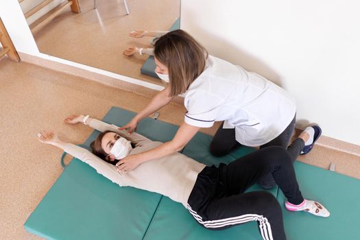 Physiotherapist doing rehabilitation exercises on a patient's arms on a mat