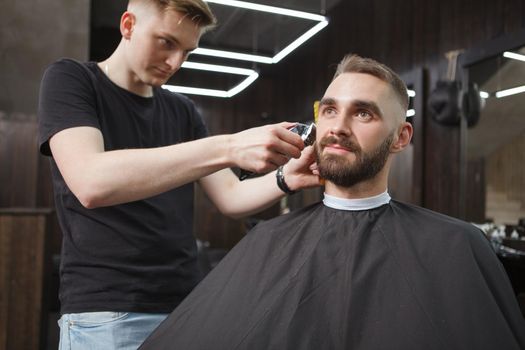 Low angle shot of a handsome man getting a new haircut, professional barber using electric trimmer