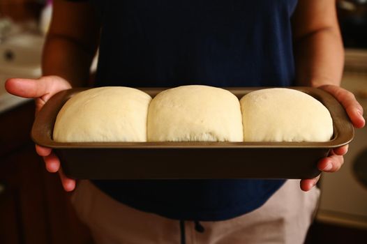 Close-up. Cropped view of the hands of a housewife holding a baking container with suitable yeast dough for bread. Culinary. Preparing a healthy homemade whole grain bread