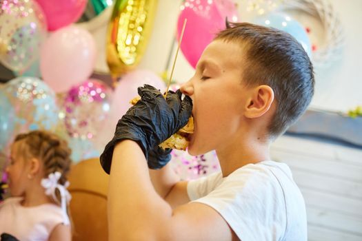 The handsome little boy eating burger in black rubber gloves