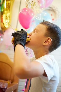 The handsome little boy eating burger in black rubber gloves