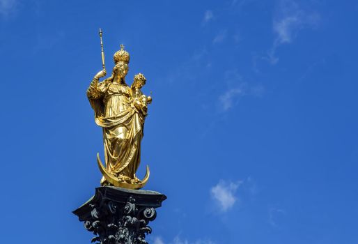 The statue of the Mariensäule on Marienplatz in Munich. The Mariensäule is a golden colored statue depicting the Madonna and Child Jesus standing on a crescent moon