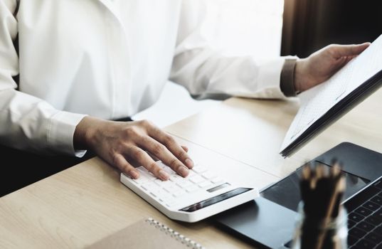 Business woman using calculator to review balance sheet annual using document and laptop computer to calculating budget. audit and Check integrity before investment concept