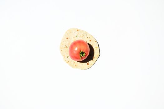 Flat lay of a ripe juicy tomato on a freshly baked homemade chapati, pita bread, flatbread, isolated over white background with copy space for advertising text. Top view, still life, food background