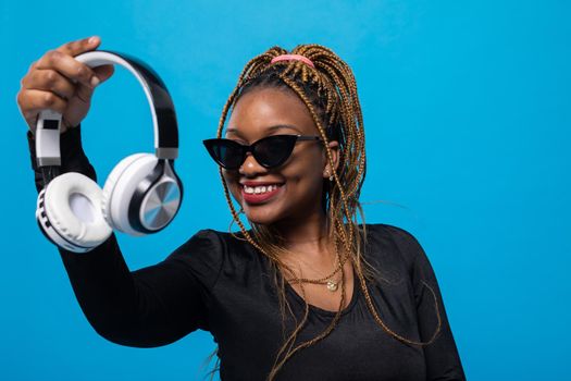 Dark-skinned girl shows everyone wireless headphones while holding them up. A college student with braided pigtails.