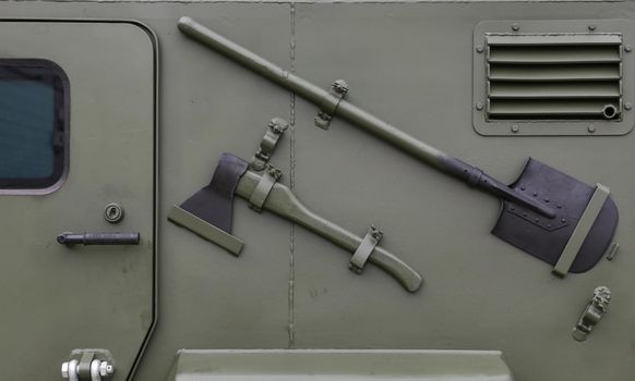 Fragment of the side of an armored vehicle with a door, a shovel, an axe. Close-up combat military equipment.