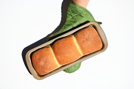 Top view of a chef's hand in a kitchen glove holding a baking dish with freshly baked hot whole grain bread, isolated on white background with copy ad space for advertising text. Still life. Food