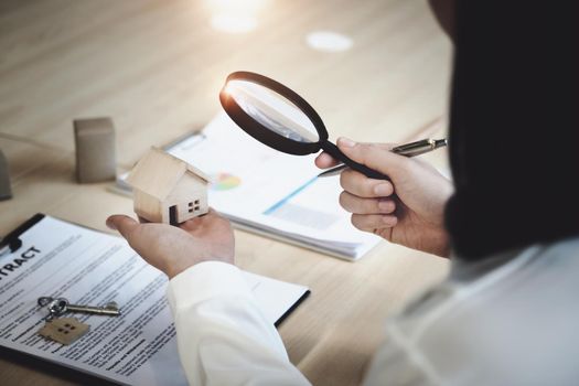 Inspector Concept, a customer is holding a magnifying glass to look at each house model to check the price of a home loan for each model