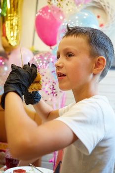 The handsome little boy eating burger in black rubber gloves