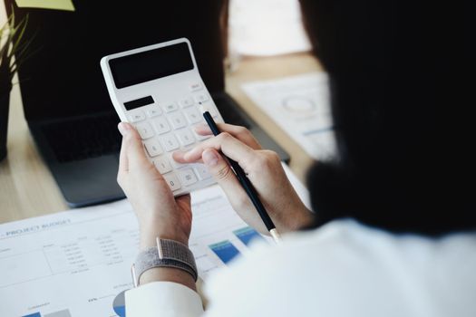 Business woman using calculator to review balance sheet annual using document and laptop computer to calculating budget. audit and Check integrity before investment concept