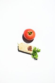 Top view of a ripe juicy tomato next to a parsley wrapped in a pita bread or flatbread, isolated on white background with copy space for advertising text. Still life. Flat lay. Food composition