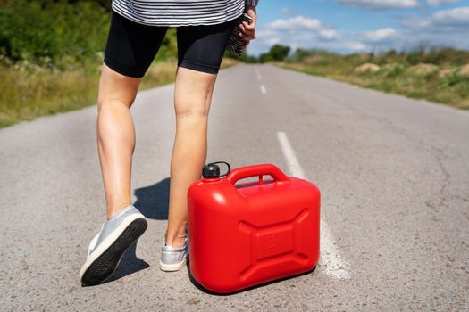 A car parked on the side of the road, an empty red canister. The girl stops on the road to fill up the car. Fuel shortage - oil, diesel, gasoline