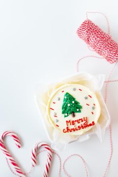 Christmas cake with the inscription merry christmas, decorated with icing, on a white background with candy canes and a red thread for gifts, preparation for the holiday