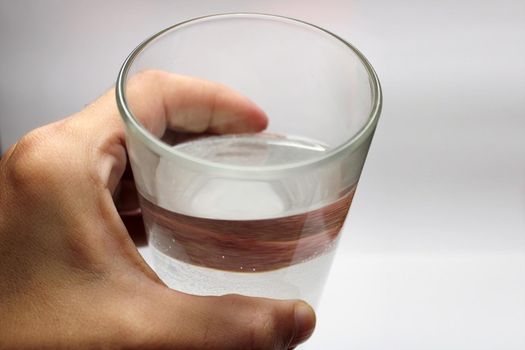 A glass of water in a hand close-up on a light background with copy space.