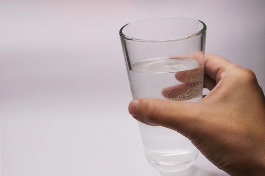 A glass of water in a hand close-up on a light background with copy space.