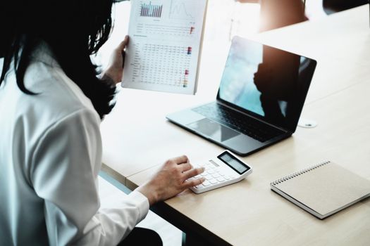 Business woman using calculator to review balance sheet annual using document and laptop computer to calculating budget. audit and Check integrity before investment concept