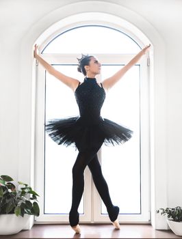 Young ballet dancer practicing before performance in black tutu, classical dance studio, copy space