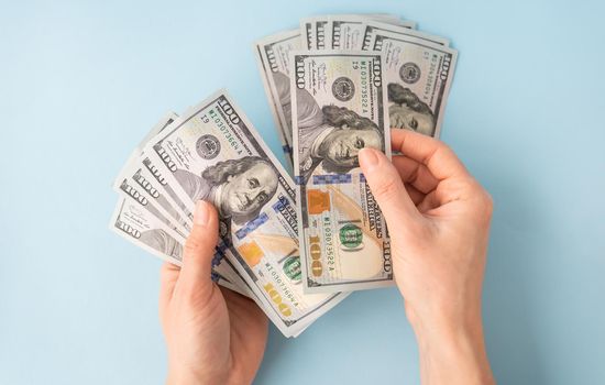 Female hands counting 100 dollar bills isolated on a blue background