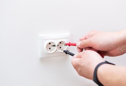 Measuring the voltage in the socket with a professional digital multimeter. Profession electrician, the process of installing sockets. Close-up, selective focus, noise