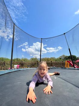Smiling little girl lying on her stomach on a trampoline. High quality photo
