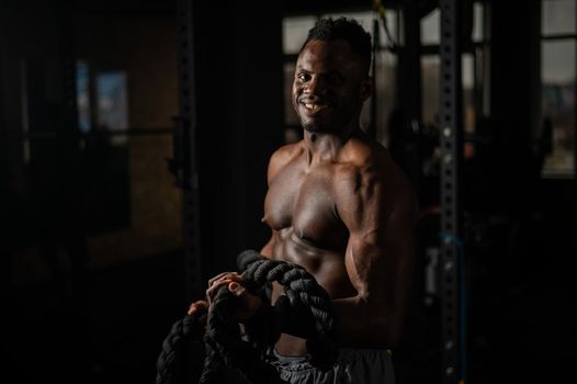 Muscular african american man posing with rope in gym