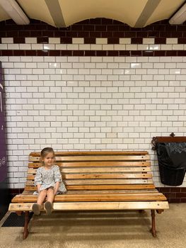 Little girl sitting on a wooden bench in the subway. High quality photo