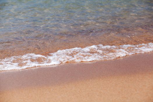 A soft wave runs on a sandy shore on a summer day. Empty space can be used as background for display or montage your top view products.