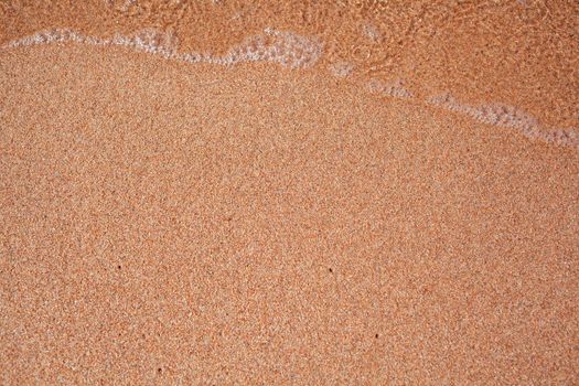 A soft wave runs on a sandy shore on a summer day. Empty space can be used as background for display or montage your top view products.