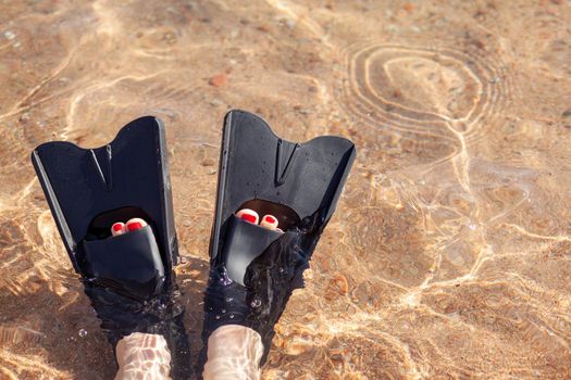 A woman in black flippers splashes near the shore. Fins stick out of the water. Swimming equipment. Summer holidays, fun, exploring the sea world concept. Space for copy.