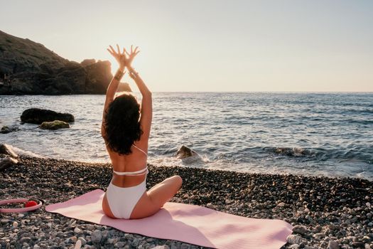 Young woman in swimsuit with long hair practicing stretching outdoors on yoga mat by the sea on a sunny day. Women's yoga fitness pilates routine. Healthy lifestyle, harmony and meditation concept.