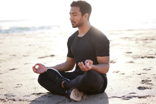 Its a matter of balance. Full length shot of a handsome young male athlete meditating on the beach