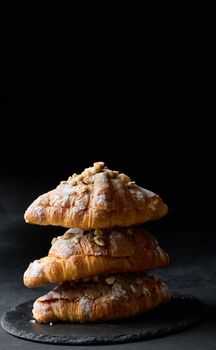 Baked croissant on a  board and sprinkled with powdered sugar, black table. Appetizing pastries for breakfast	