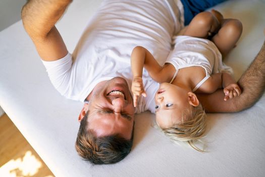 Little girl lies next to a laughing dad. High quality photo
