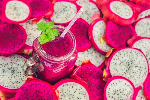 Smoothies of red organic dragon fruit and pieces of dragon fruit on an old wooden background.