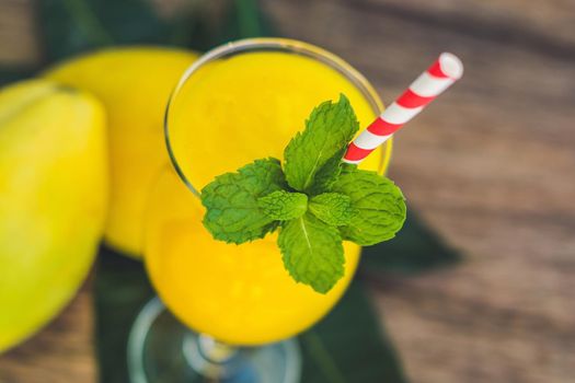 Juicy smoothie from mango in glass with striped red straw and with a mint leaf on old wooden background. Healthy life concept, copy space.